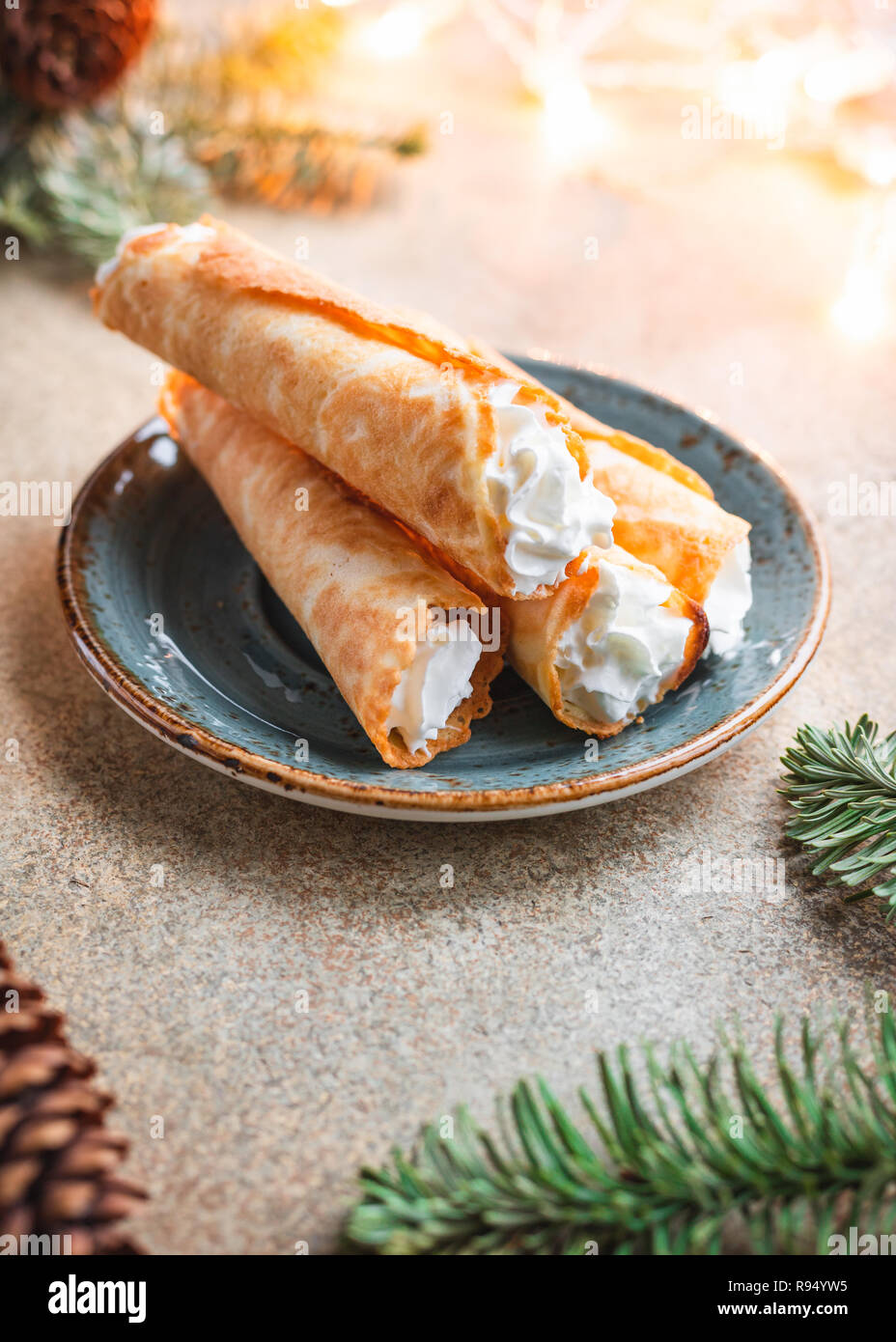 Traditional Christmas Norwegian cookies Krumkake with whipped cream among winter decor. Stock Photo