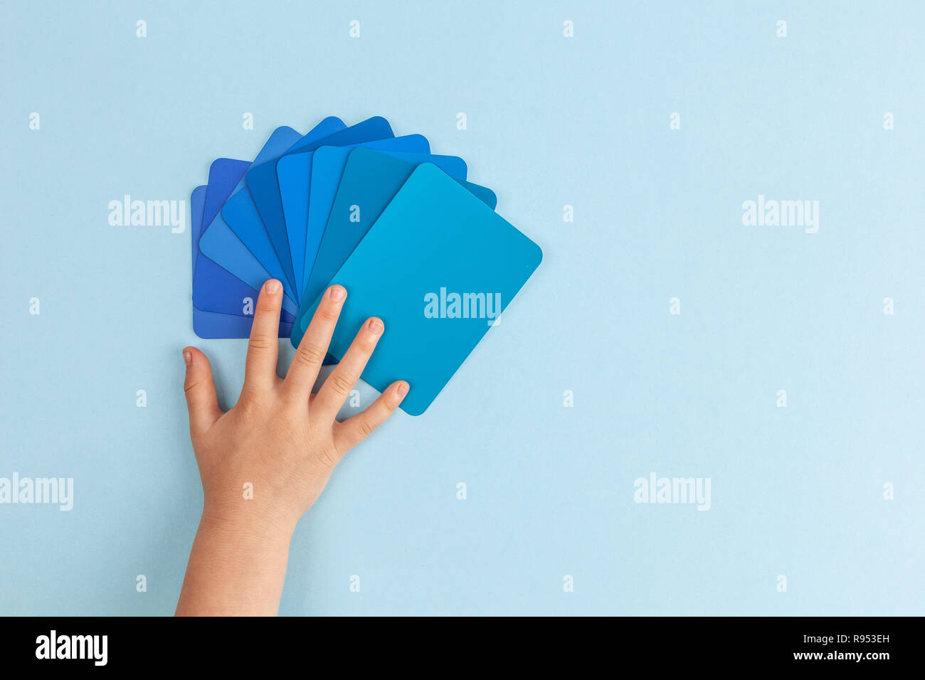 Child's hand touching color samples cards - hues of blue. Top view with copy space Stock Photo