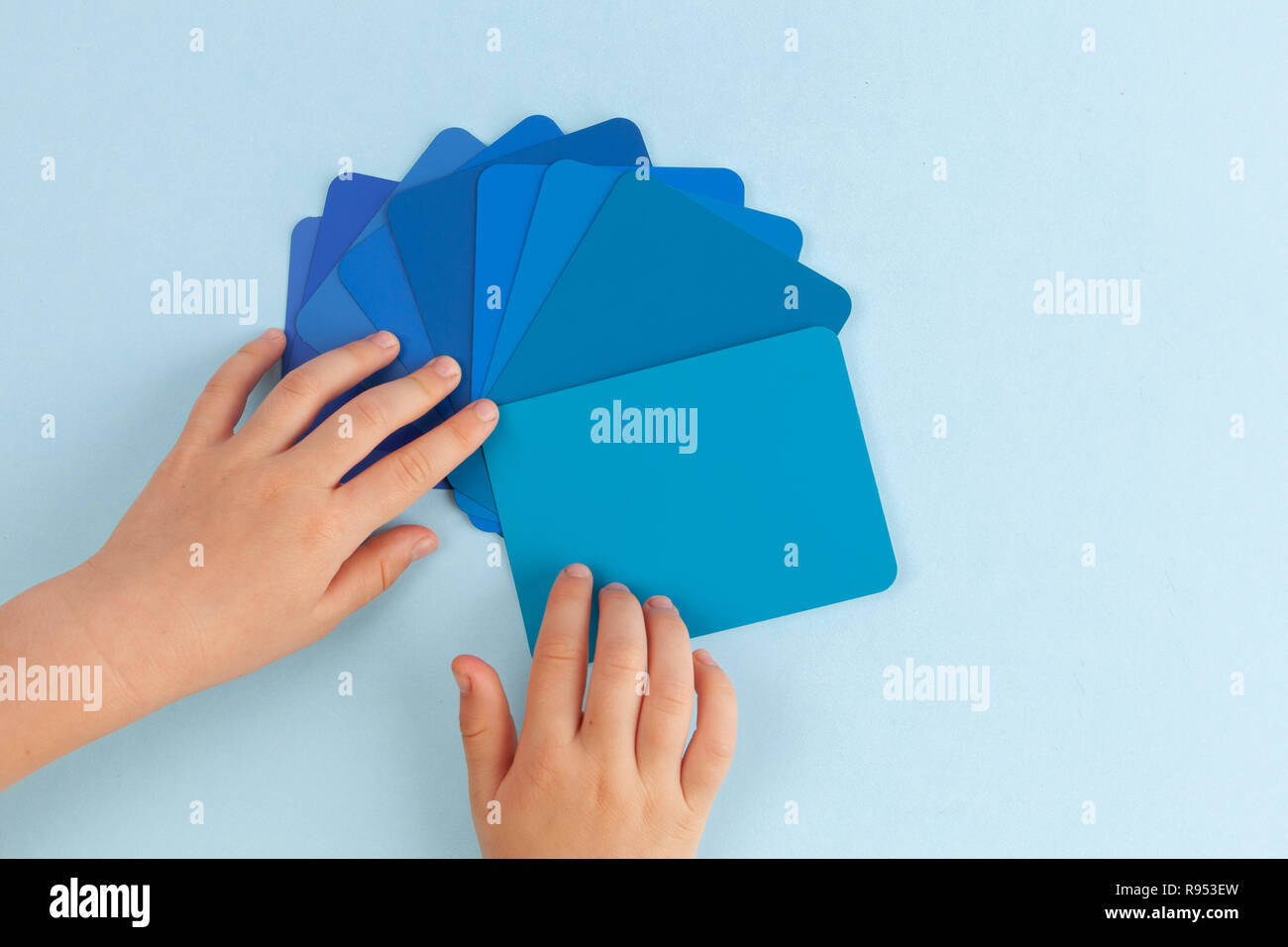 Child's hand playing with color sample cards - hues of blue. Top view with copy space Stock Photo