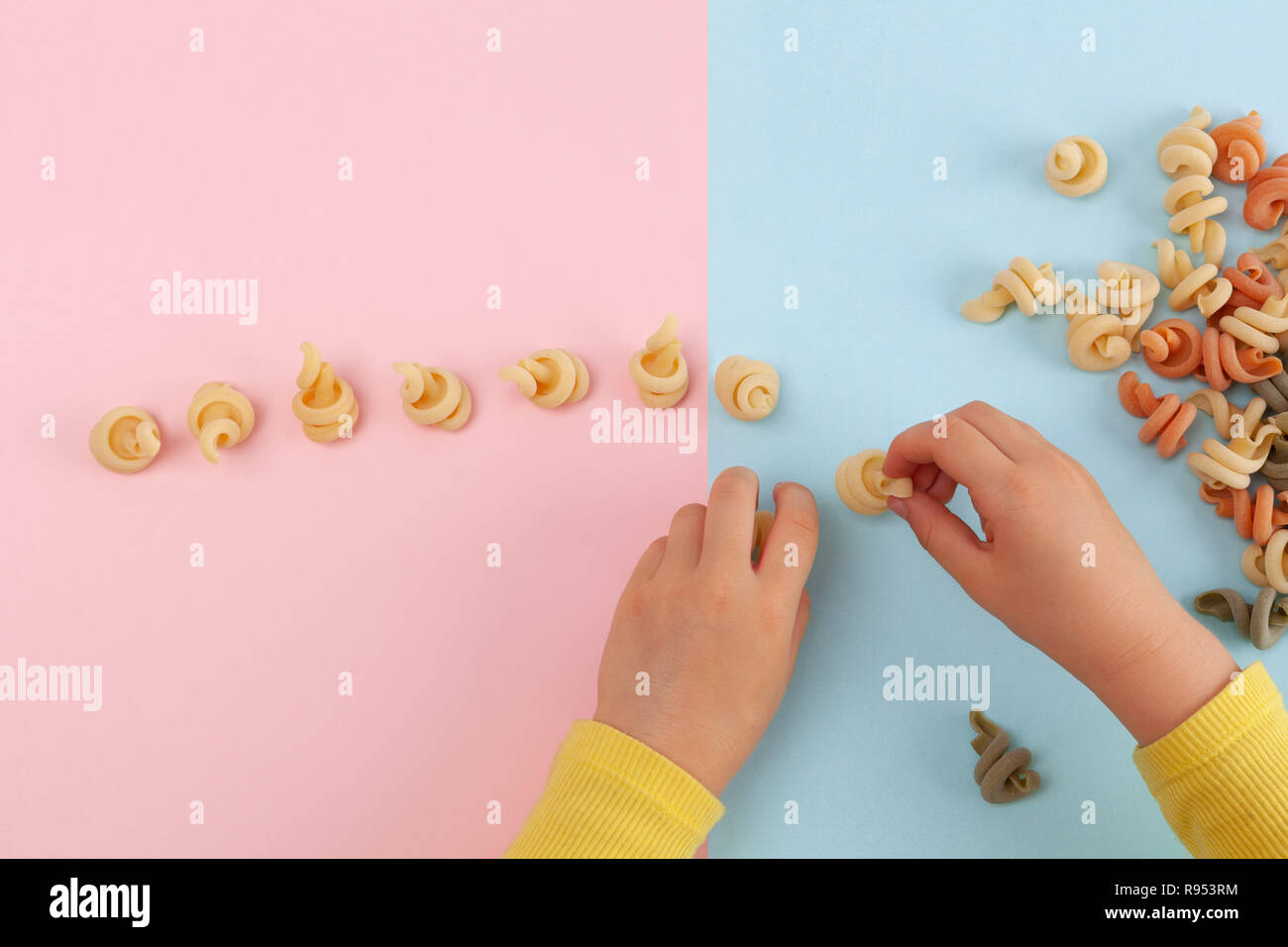 Child's hands playing with Funghetto veggie pasta on colored table with copy space Stock Photo