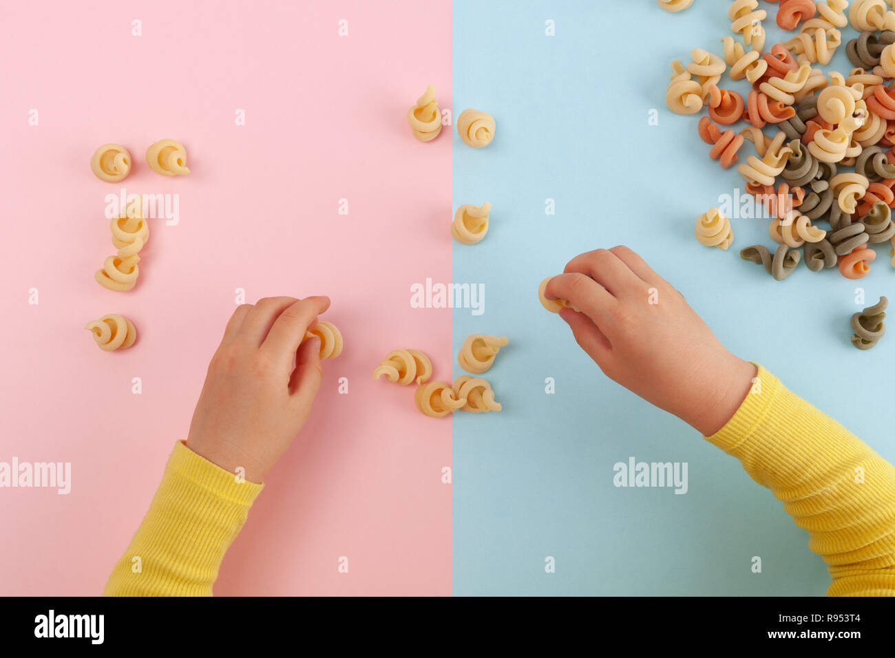 Child's hands with yellow sleeves playing with raw pasta - top view Stock Photo