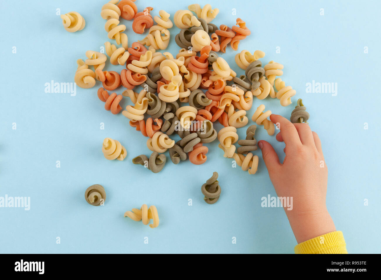 Child playing with Funghetto veggie pasta on light blue background Stock Photo