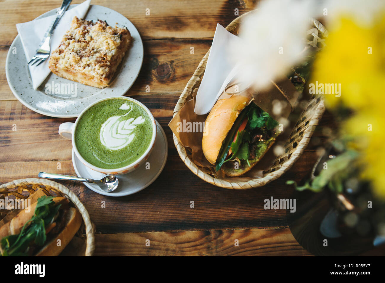 Healthy breakfast in the restaurant: cup of green tea with milk, dessert and two sandwiches with vegetables and herbs on wooden table Stock Photo