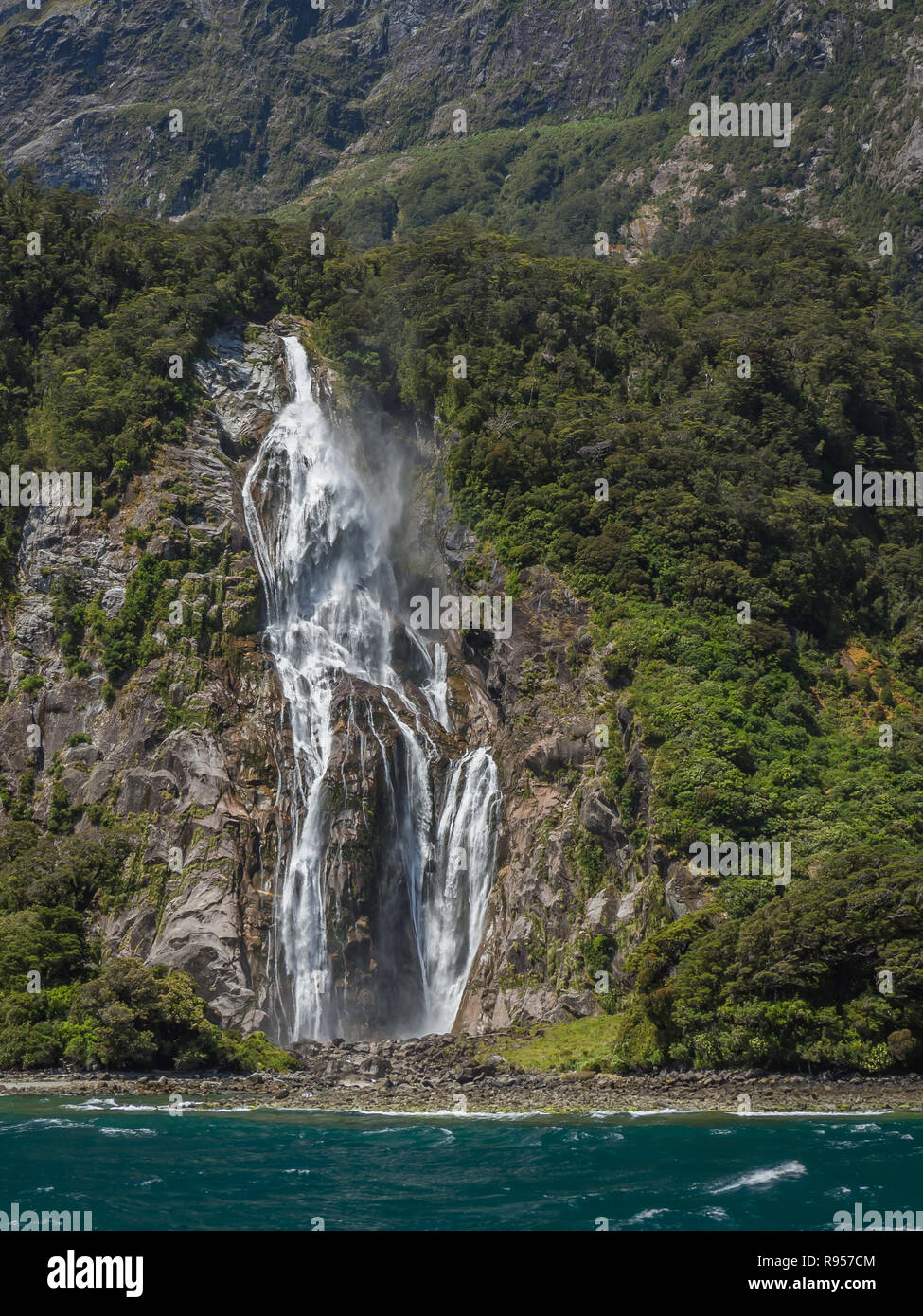Stirling Falls releases a torrent of water down a rocky mountainside into Milford Sound in Fiordland National Park on the South Island of New Zealand Stock Photo