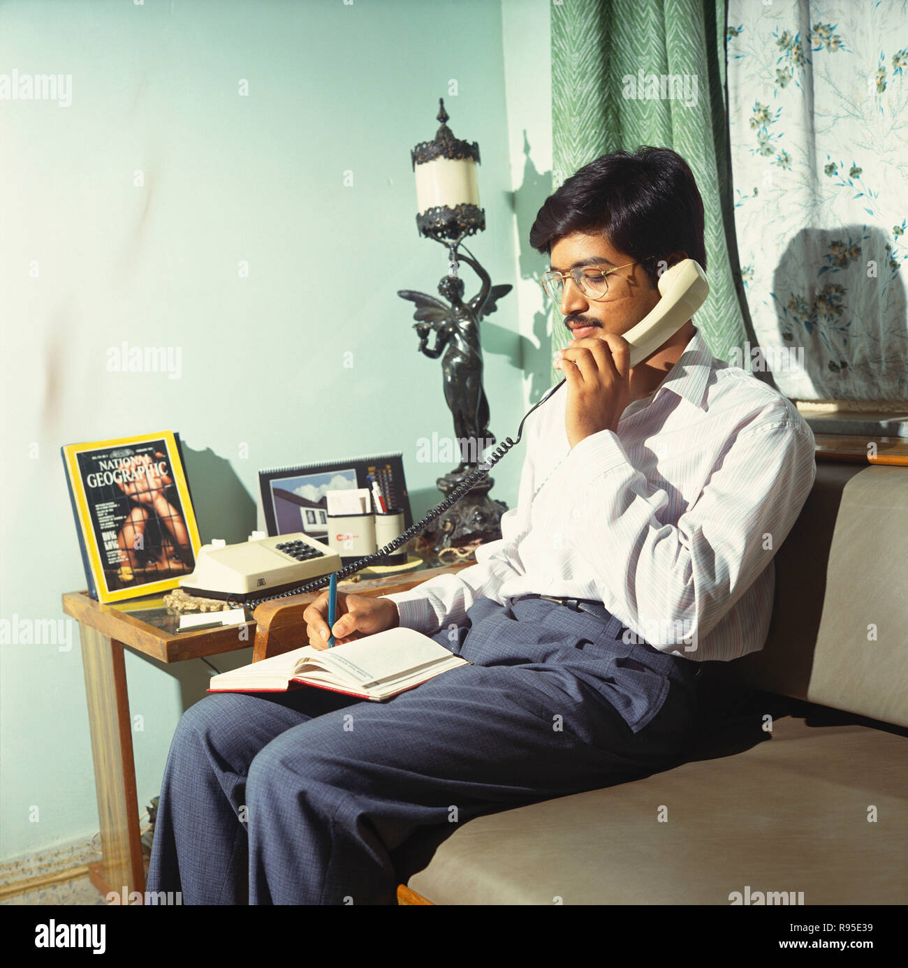 Man Holding Telephone and Writing on Book Stock Photo