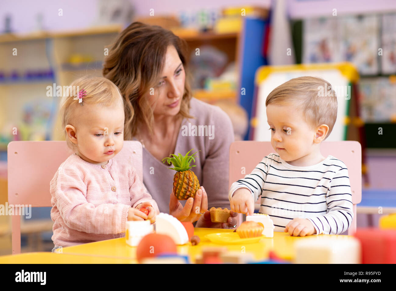 Preschool teacher with babies toddlers playing with colorful toys at kindergarten Stock Photo
