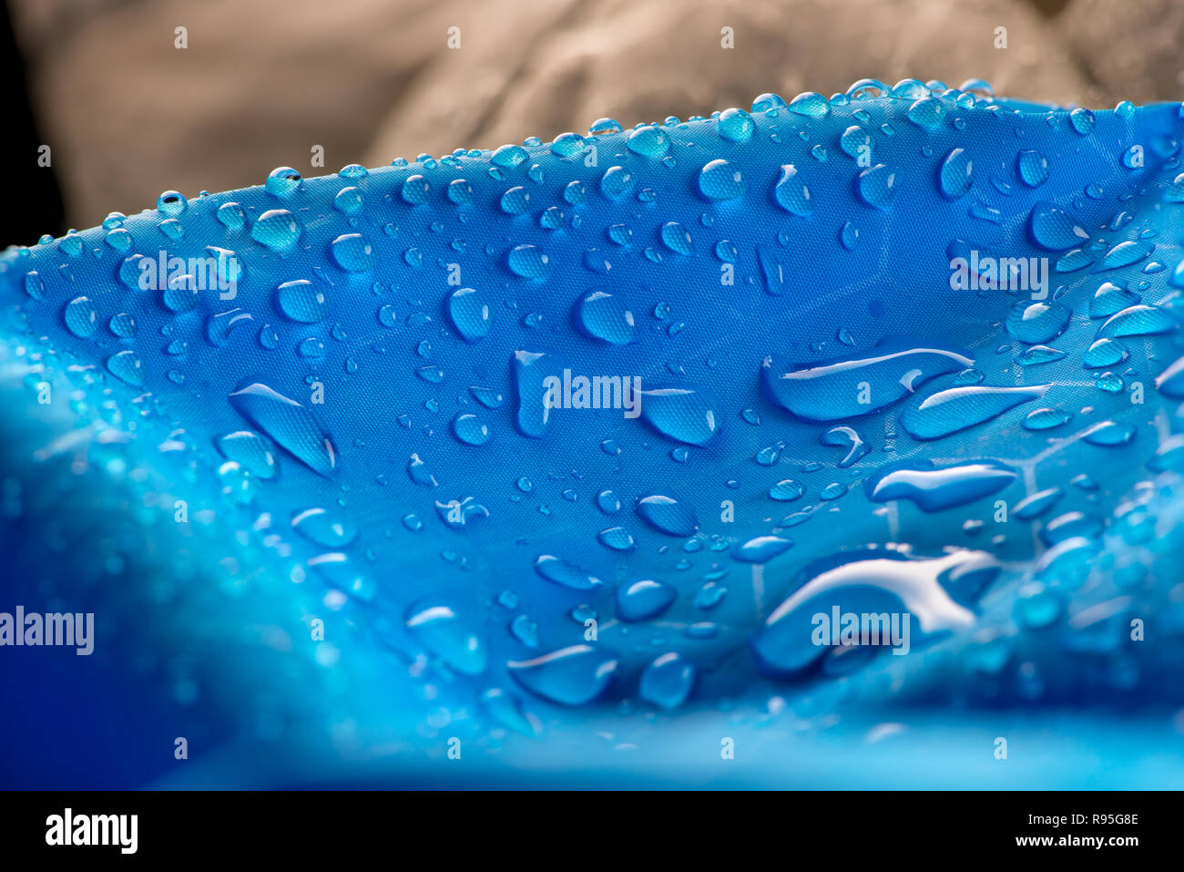 Water drops on waterproof blue nylon fabric. Macro detail view of woven synthetic waterproof clothing. Heavy blurred foreground. Rain Drops on Water R Stock Photo