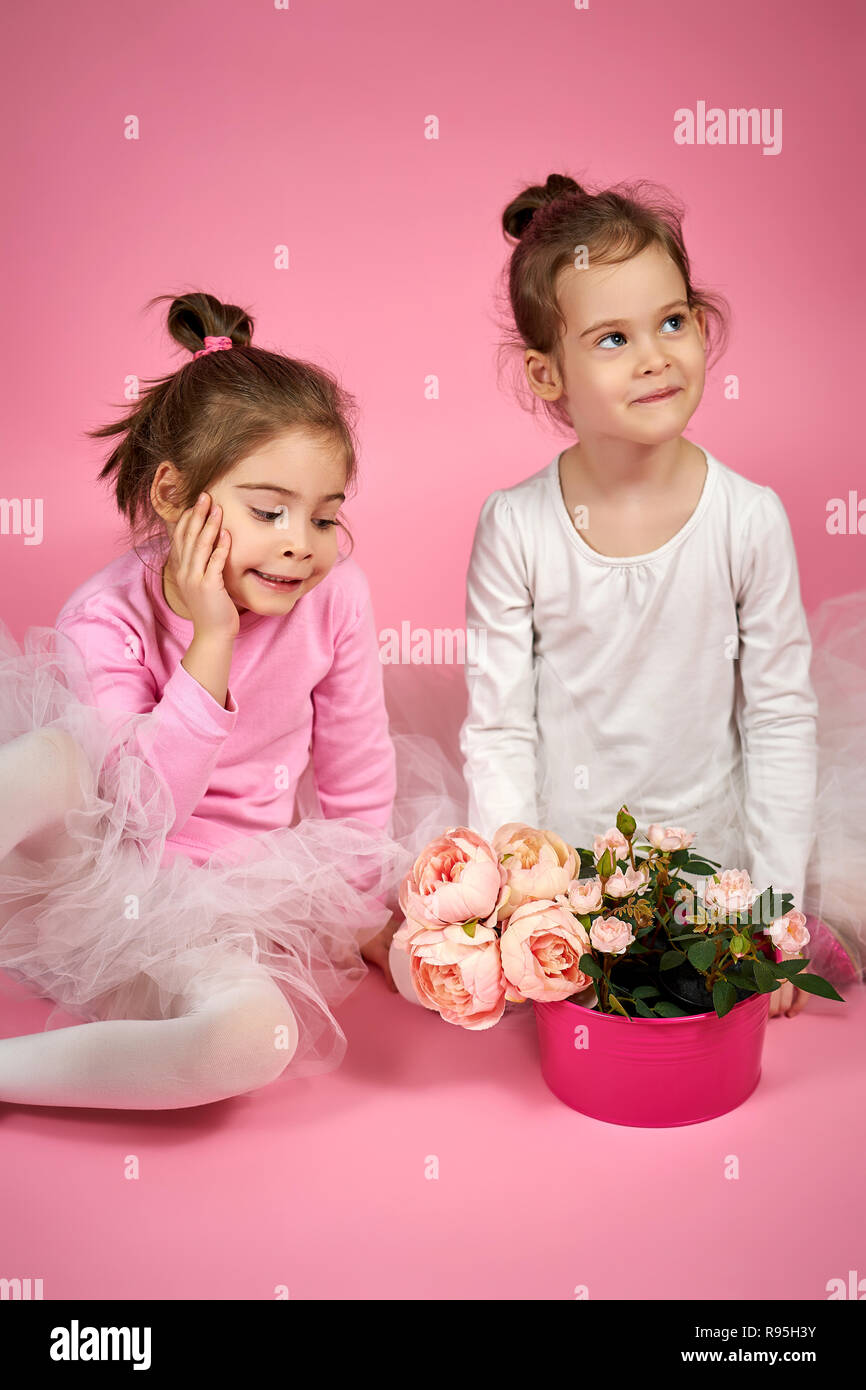 two cute little girls in white tulle skirts with a bouquet of flowers on a pink background Stock Photo