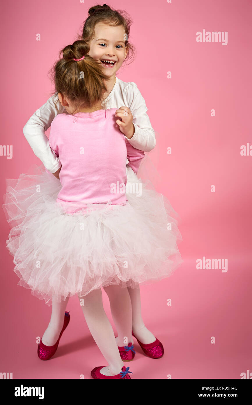 two cute little girls in white tulle skirts on a pink background Stock Photo
