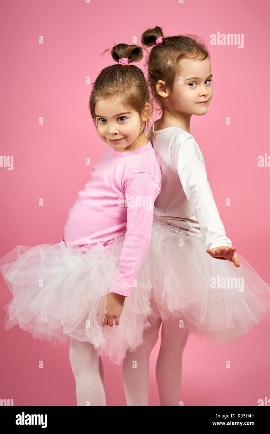 two cute little girls in white tulle skirts on a pink background Stock Photo