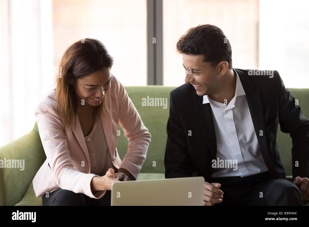 Funny diverse colleagues using laptop sitting on couch at work Stock Photo
