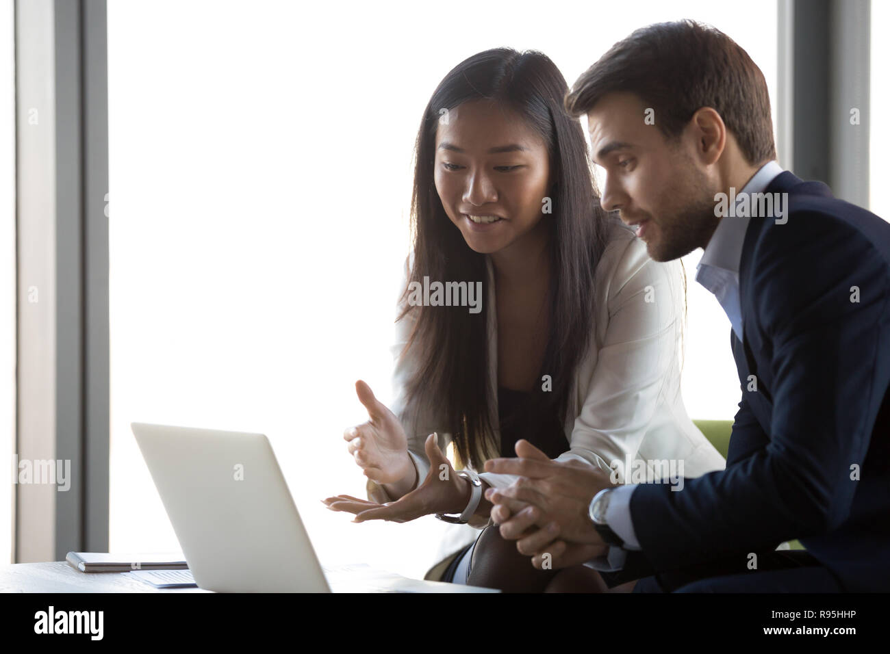 Attractive positive asian female working with caucasian man usin Stock Photo