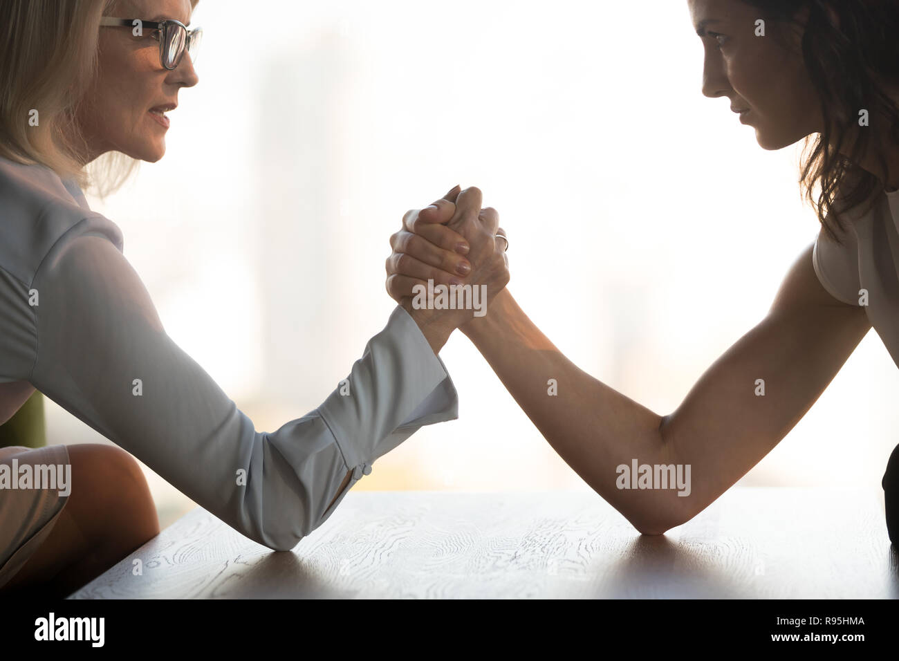 Young brunette and aged blond businesswomen arm wrestling Stock Photo