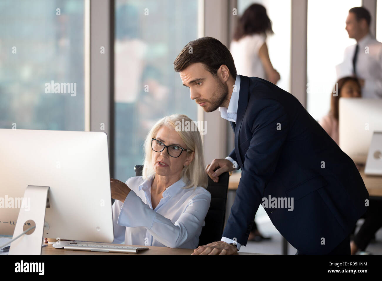 Young employee helps middle aged colleague learn corporate progr Stock Photo