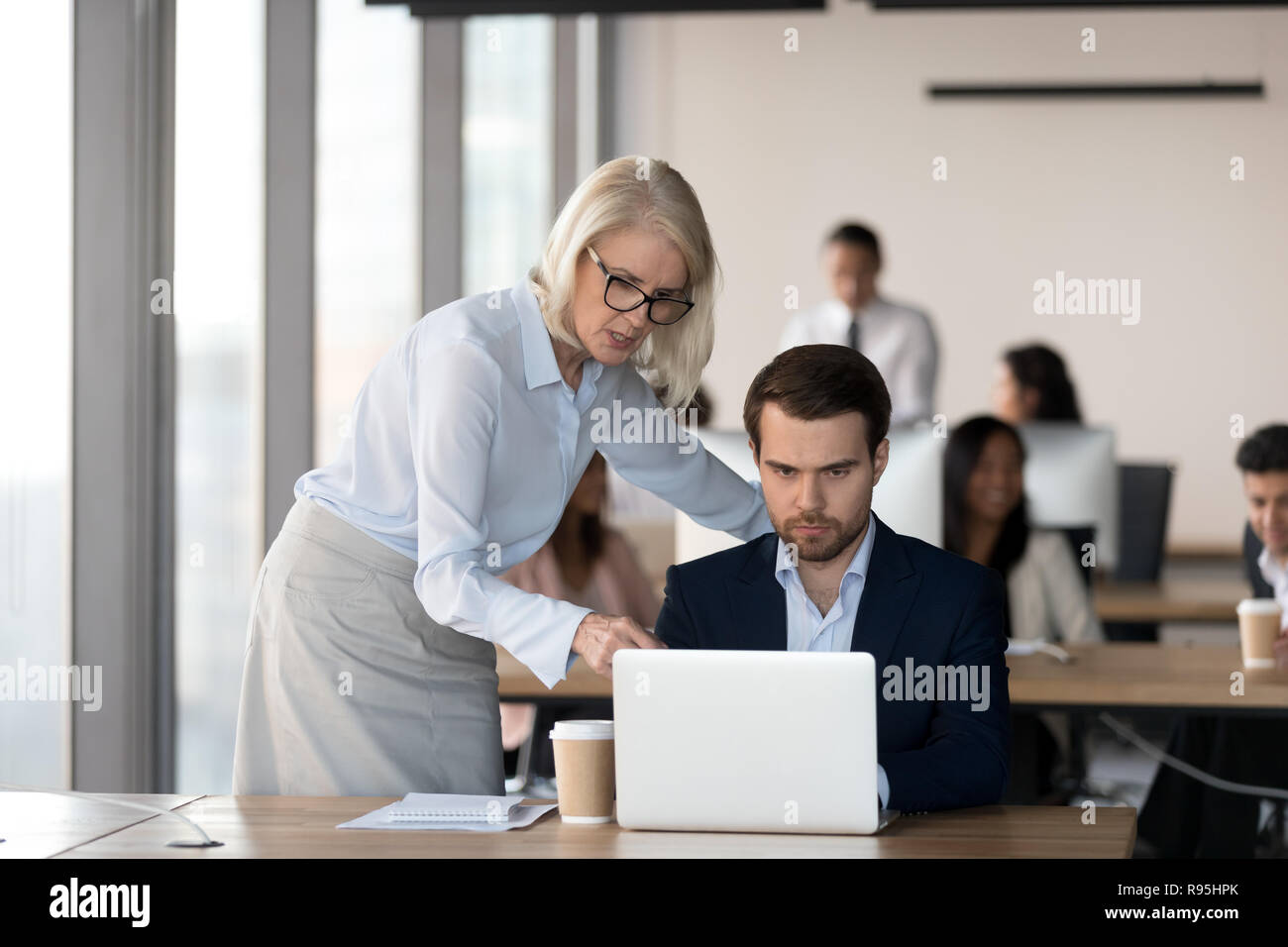 Middle aged executive manager helping to male colleague Stock Photo