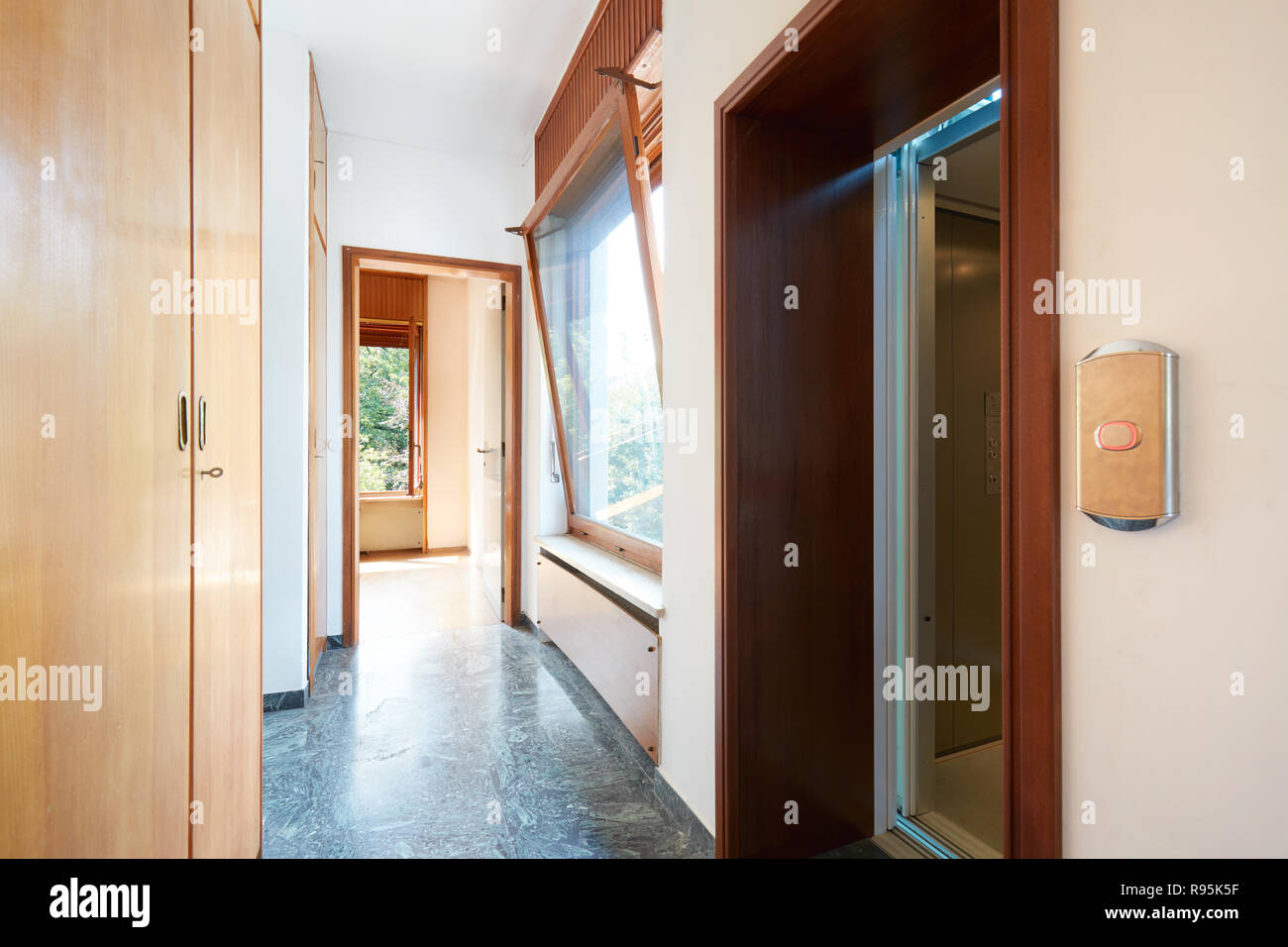 Corridor with wooden wardrobe, window and elevator door in country house Stock Photo