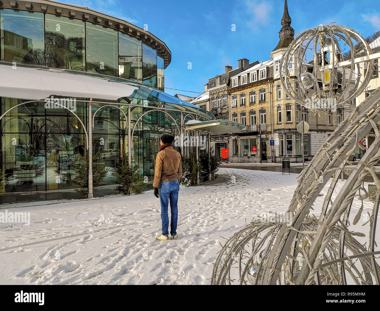 Caucasian young man standing next to the tourist office in the city center of Spa, Belgium, which is covered in snow. Spa is famous for its springs. Stock Photo