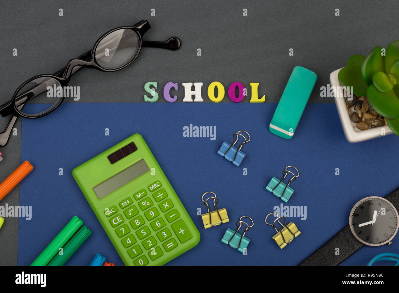 School set with blue paper, text "School" of wooden letters, calculator, markers, eyeglasses, watch and other stationery on grey background Stock Photo
