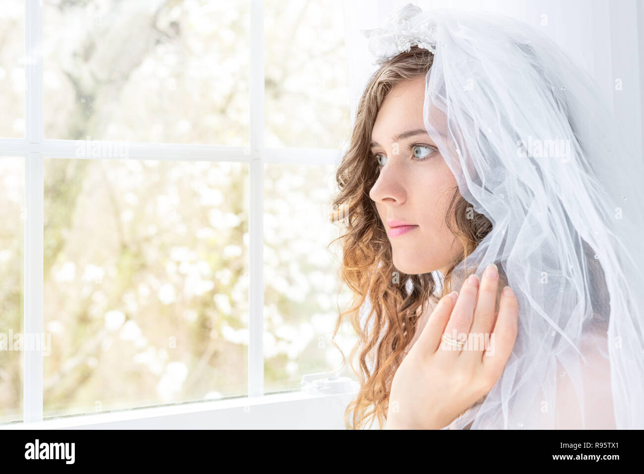 Closeup side, profile portrait of young female person, woman, bride, wedding dress, veil, face, pearl necklace, hair, standing, looking through glass  Stock Photo