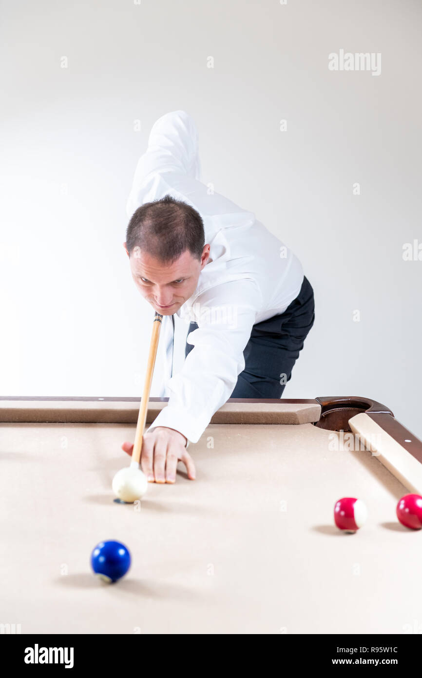 Young man, businessman in tie, white shirt, pants holding cue by pool table, playing game of snooker, billiard, billiards, striking white ball, many c Stock Photo