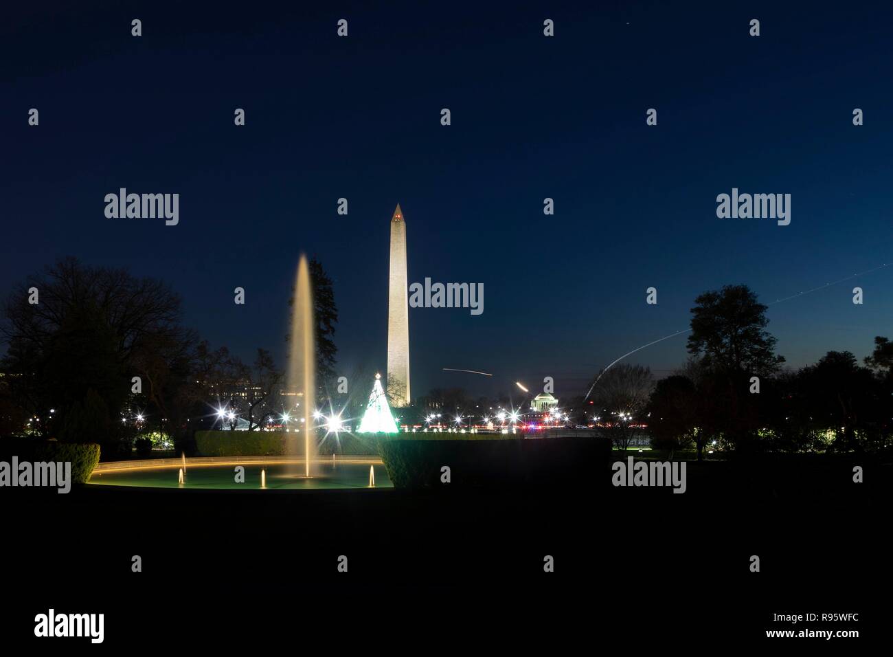 View of the Washington Monument and National Mall from the South Lawn of the White House decorated for Christmas and lighted at night December 12, 2018 in Washington, DC. The light streaks are commercial airplanes taking off from Reagan National Airport on the Potomac River. Stock Photo