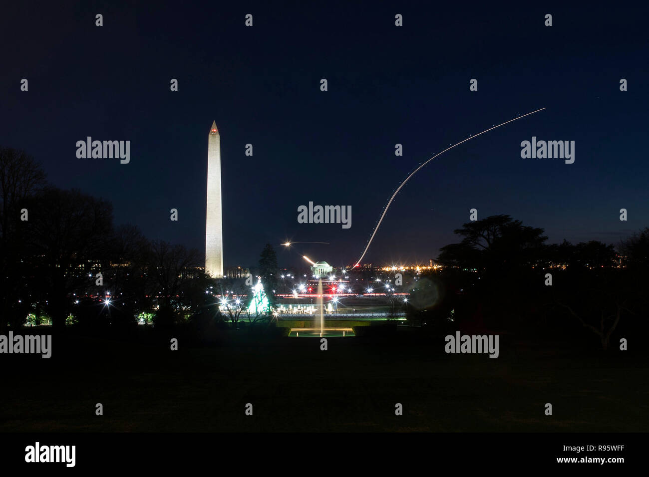 View of the Washington Monument and National Mall from the South Lawn of the White House decorated for Christmas and lighted at night December 12, 2018 in Washington, DC. The light streaks are commercial airplanes taking off from Reagan National Airport on the Potomac River. Stock Photo