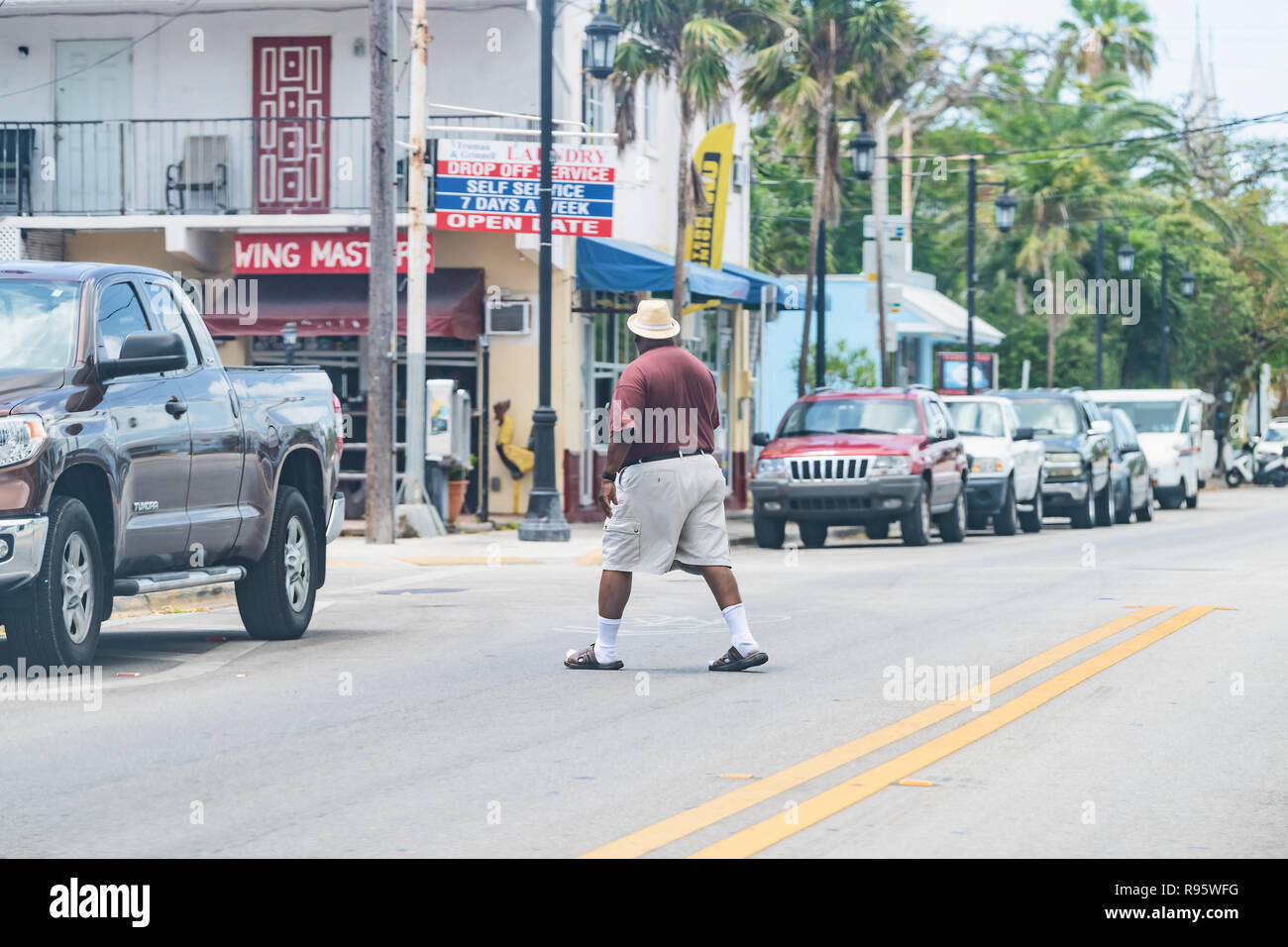 Key West, USA - May 1, 2018: Truman Avenue in Florida keys city, urban view on street, road, cars, laundry store with African American man crossing, j Stock Photo