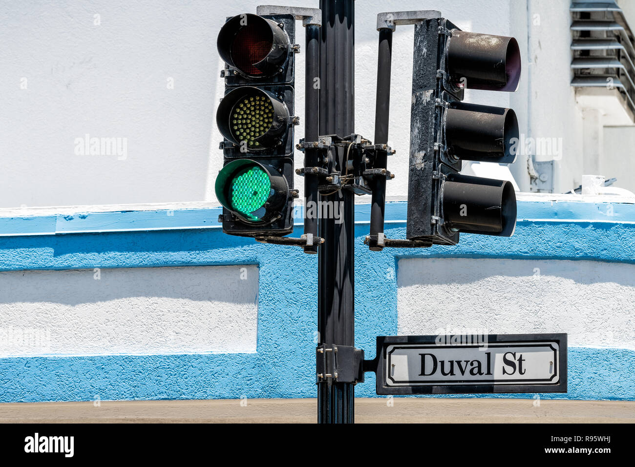 Closeup of Duval St street road traffic sign in old town of Key West, Florida, Fl in city, urban view with green light against blue, white building in Stock Photo