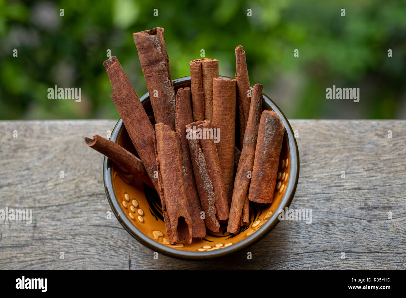 Top view of a colorful little bowl on wooden board containing cinnamon - cinnamonum serum-a seasoning ingredient in focus. Green background. Stock Photo