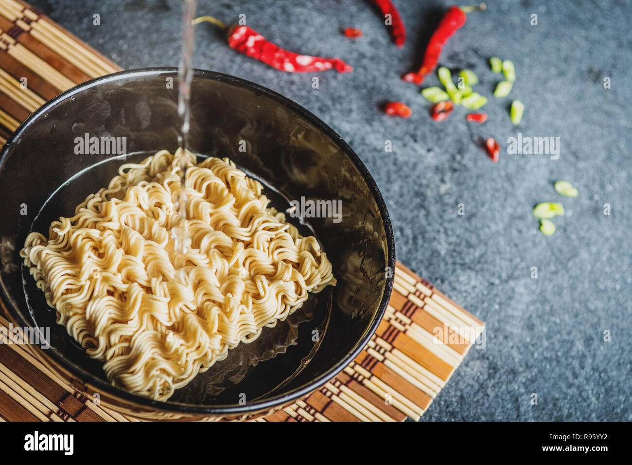 Black bowl of asian instant noodles with hot water and red chili peppers and green onion and chopsticks Stock Photo