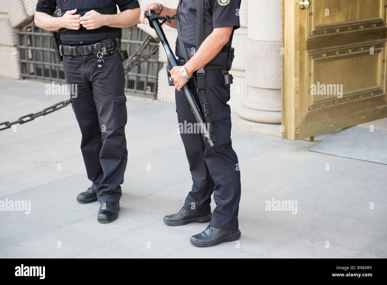 Two male policemen on duty standing before the entrance of a tourist place. They are seen wearing black uniform with one of them holding stick in thei Stock Photo