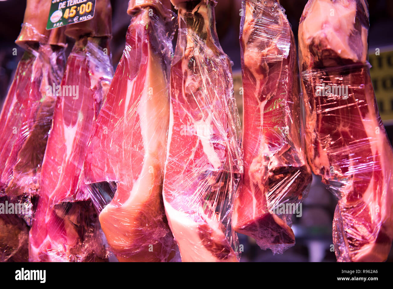 Raw, uncooked meat being displayed at a meat store for sale. The meat is seen hanging from the hooks and looks very fresh and healthy. Stock Photo