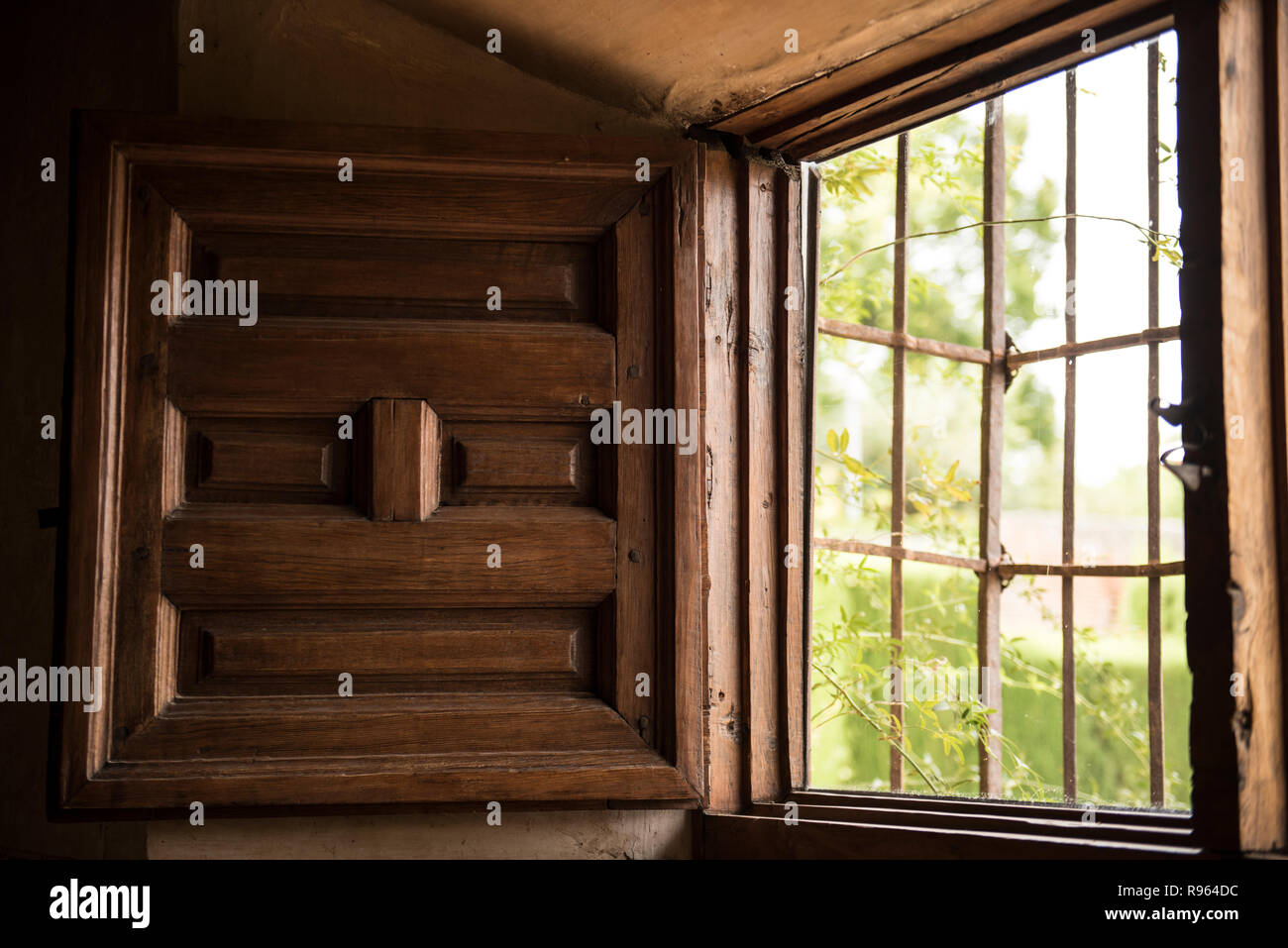 An wooden window closeup can be seen. The design looks modern day architecture, and iron bars can be seen attached to it. Lush green trees are seen ou Stock Photo