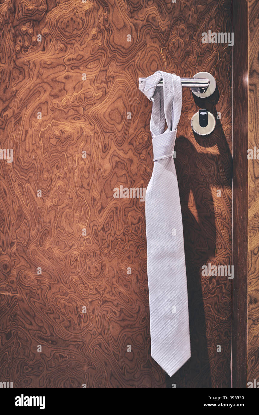 Tie hanging on a hotel closed door handle, do not disturb informal sign, retro color toning applied, selective focus. Stock Photo