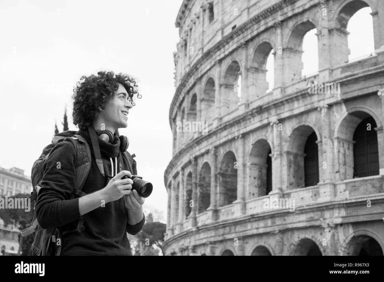 Black and white image of young tourist with a camera and backpack taking pictures of Colosseum in Rome, Italy. Young tourist taking pictures of Coloss Stock Photo