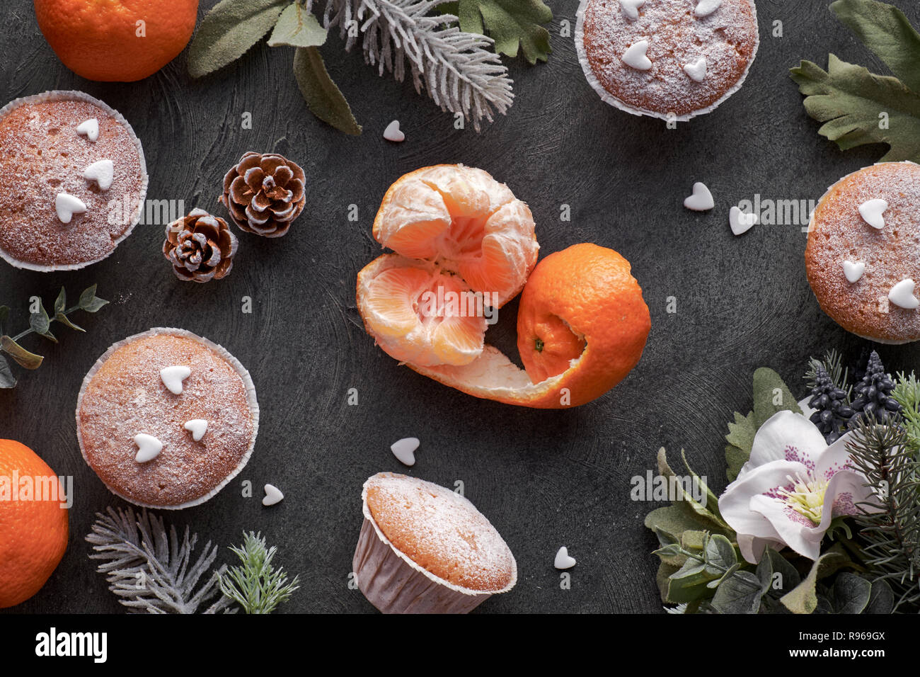 Top view of the table with satsumas, sugar-sprinkled muffins and Christmas star cookies on dark textured background Stock Photo