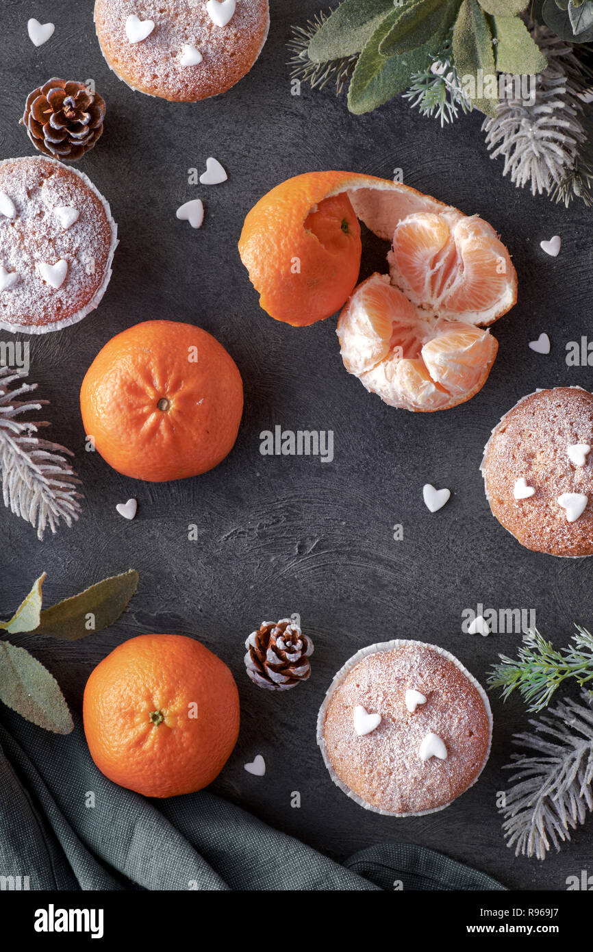 Top view of the table with satsumas, sugar-sprinkled muffins and Christmas star cookies on dark textured background Stock Photo