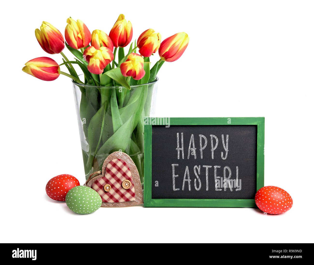 Blackboard with chalk greeting text 'Happy Easter', bunch of red stripy tulips in glass vase, Easter eggs and wooden heart isolated on white backgroun Stock Photo