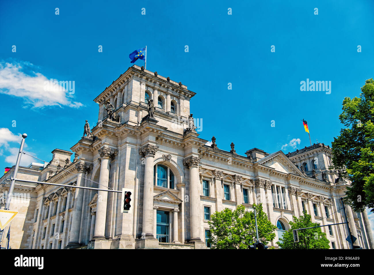 German flags waving in the wind at famous Reichstag building, seat of the German Parliament Deutscher Bundestag , on a sunny day with blue sky and clouds, central Berlin Mitte district, Germany Stock Photo