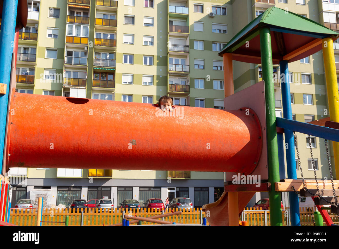 Boy child at playground peeping out of the hole of a big orange toy tube. Stock Photo