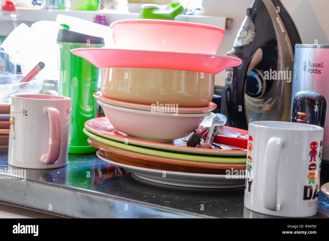 Plates, dishes and mugs piled up on a kitchen worktop ready to be washed up. Stock Photo