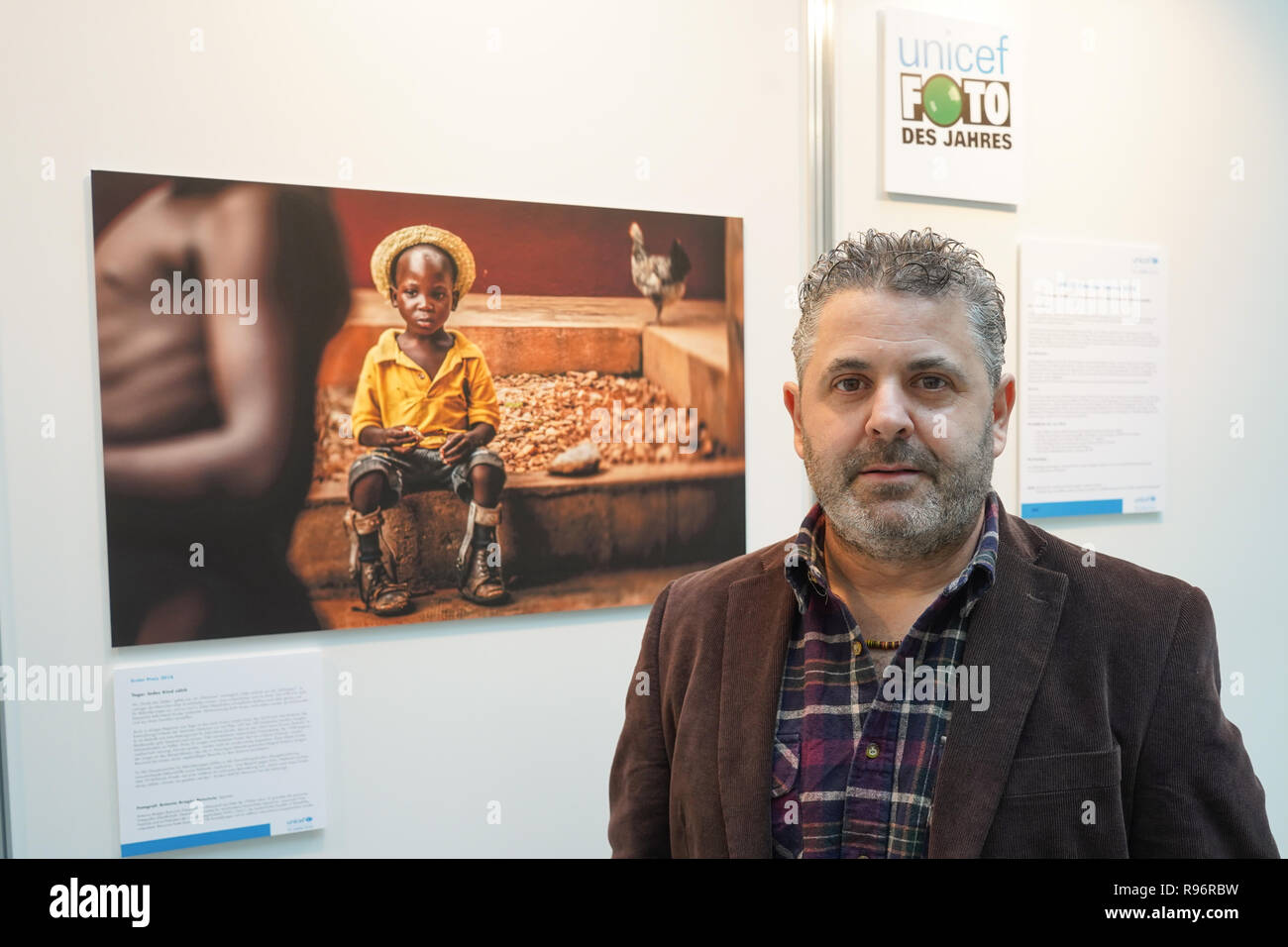 Berlin, Germany. 20th Dec, 2018. The Spanish photographer Antonio Aragon Renuncio is in front of the winning photo at the award ceremony of the photo competition 'Unicef Photo of the Year 2018'. The photo taken by Renuncio shows a boy with leg prostheses in the 'Saint Louis Orione Centre' in Togo. About 70 mentally and physically handicapped children find a home here. Credit: Jörg Carstensen/dpa/Alamy Live News Stock Photo