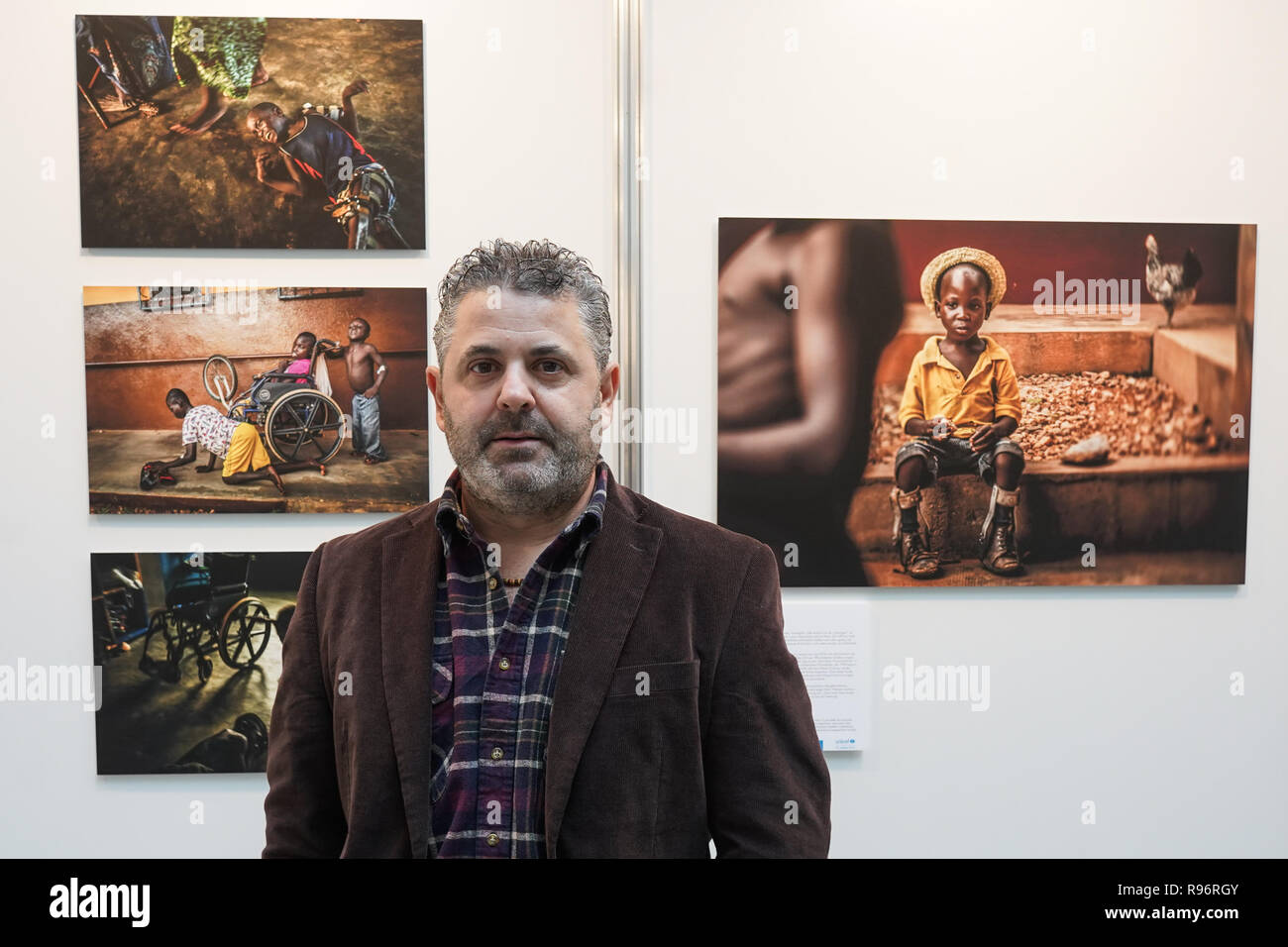 Berlin, Germany. 20th Dec, 2018. The Spanish photographer Antonio Aragon Renuncio is in front of the winning photo (r) at the award ceremony of the photo competition 'Unicef Photo of the Year 2018'. The photo taken by Renuncio shows a boy with leg prostheses in the 'Saint Louis Orione Centre' in Togo. About 70 mentally and physically handicapped children find a home here. Credit: Jörg Carstensen/dpa/Alamy Live News Stock Photo