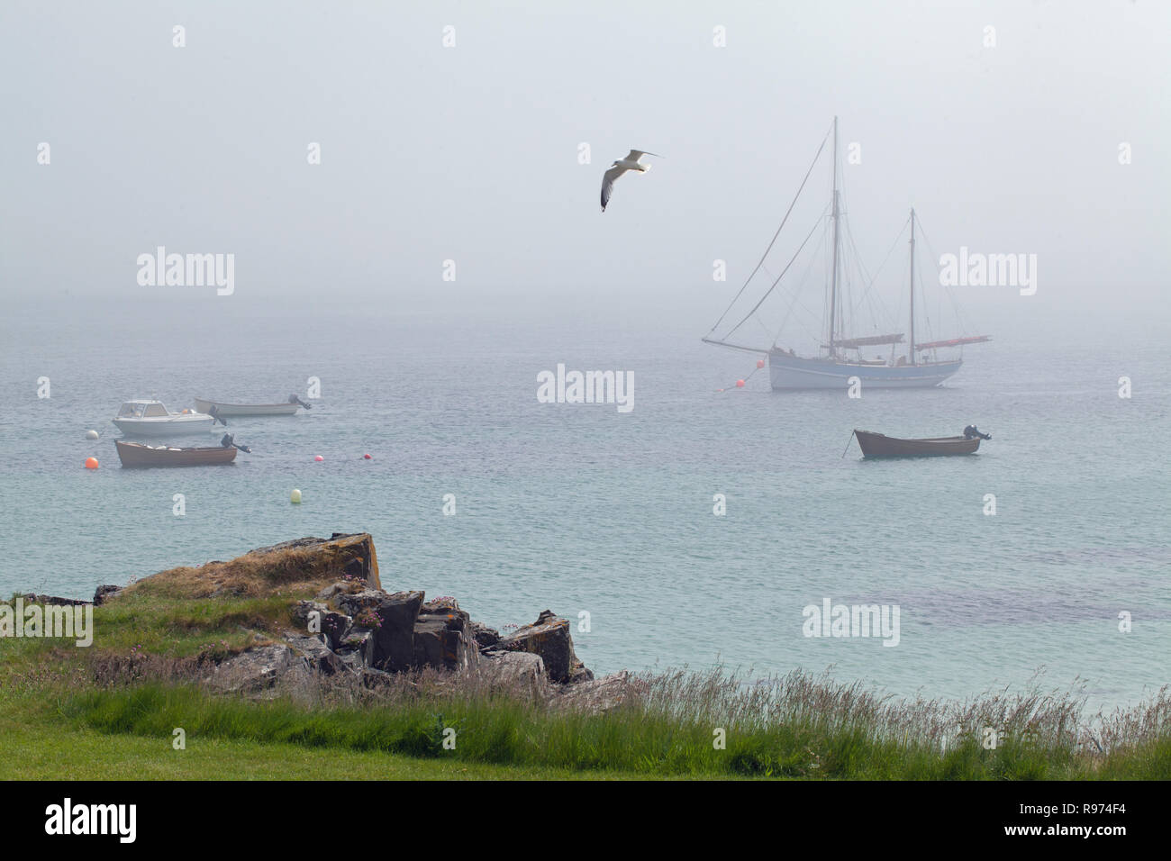 Anchored Boats.  View from The Village, St. Ronan’s Bay, Isle of Iona, across The Sound, towards Fionnphort, Mull, horizon obscured by early morning mist. Stock Photo