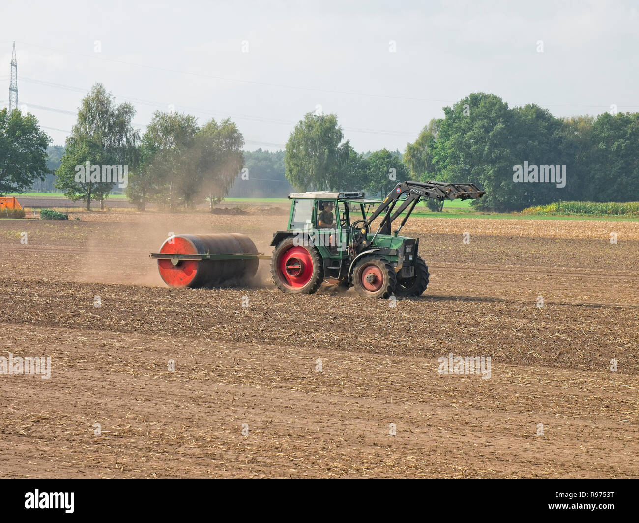 Farmer on his tractor flattening a field with his heavy barrel near Mechtersen North Germany. Stock Photo