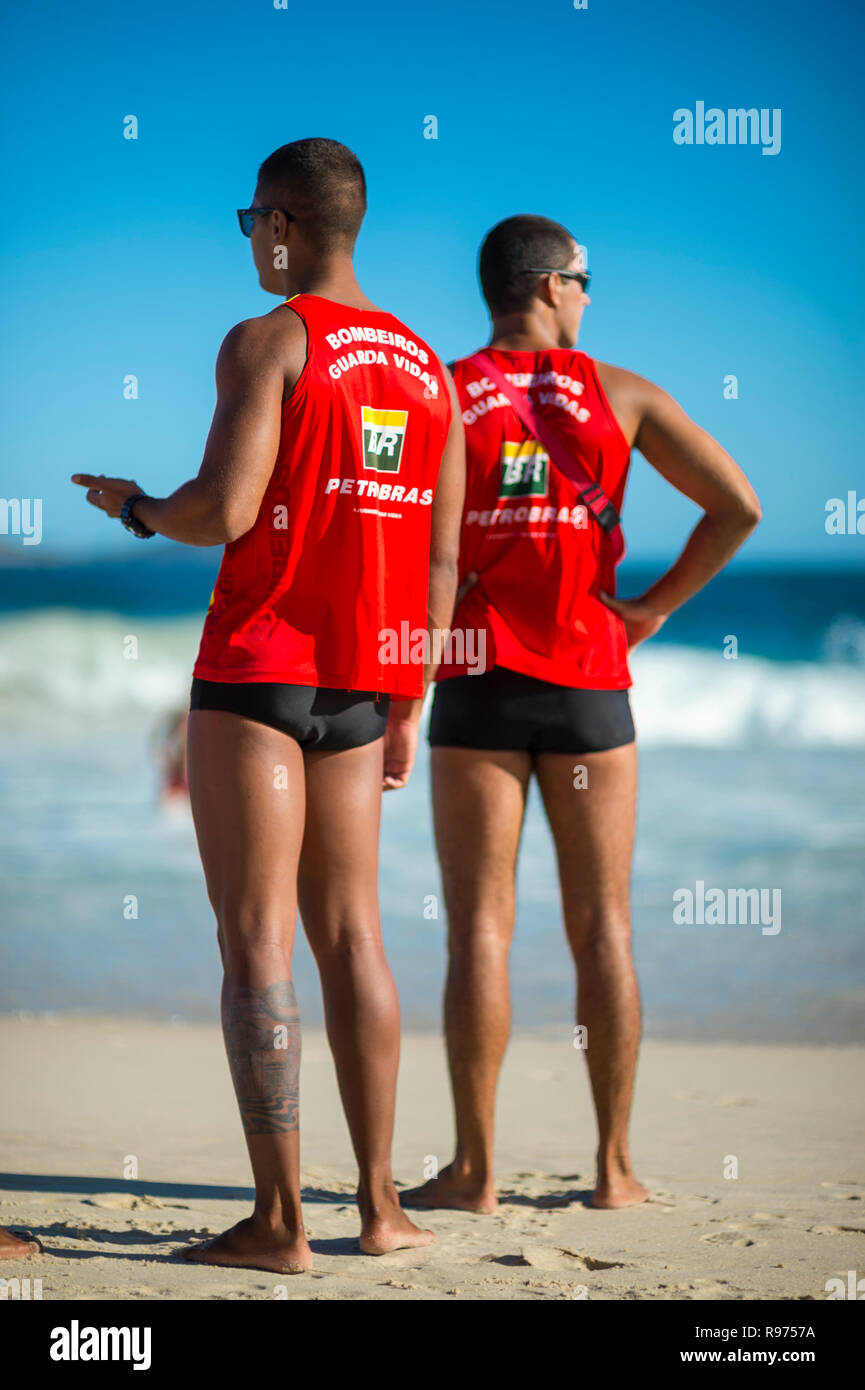 RIO DE JANEIRO - MARCH, 2018: A pair of athletic lifeguards in uniform monitor swimmers in the heavy surf on Ipanema Beach. Stock Photo