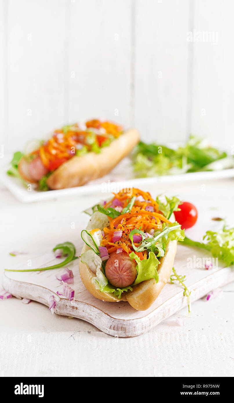 Hot dog with cucumber, carrot, tomato and lettuce on wooden background