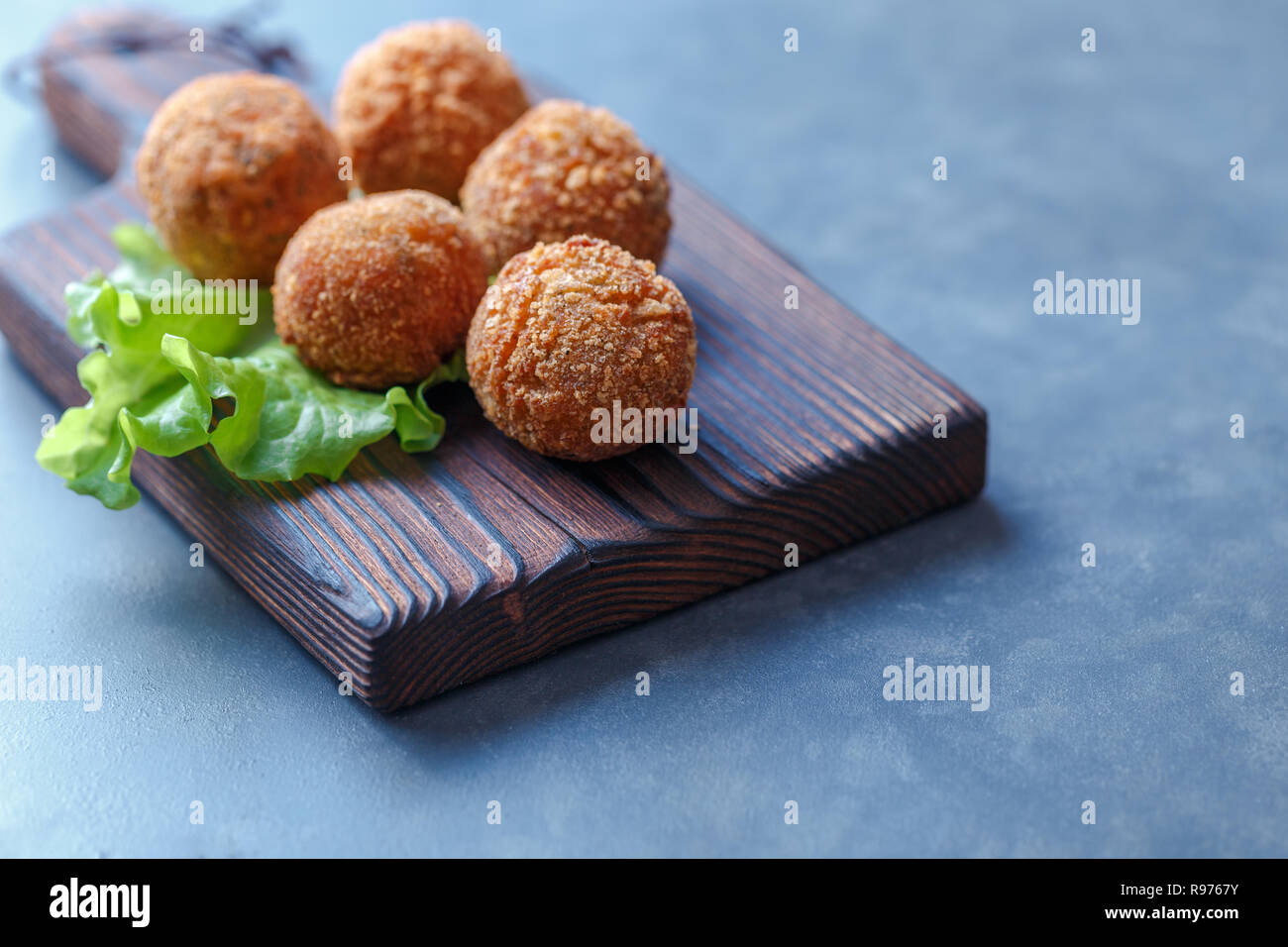 Falafel lies on a wooden cutting board. On the table lie tomatoes, cucumbers, lettuce, dill, lemon, sour cream. Stock Photo