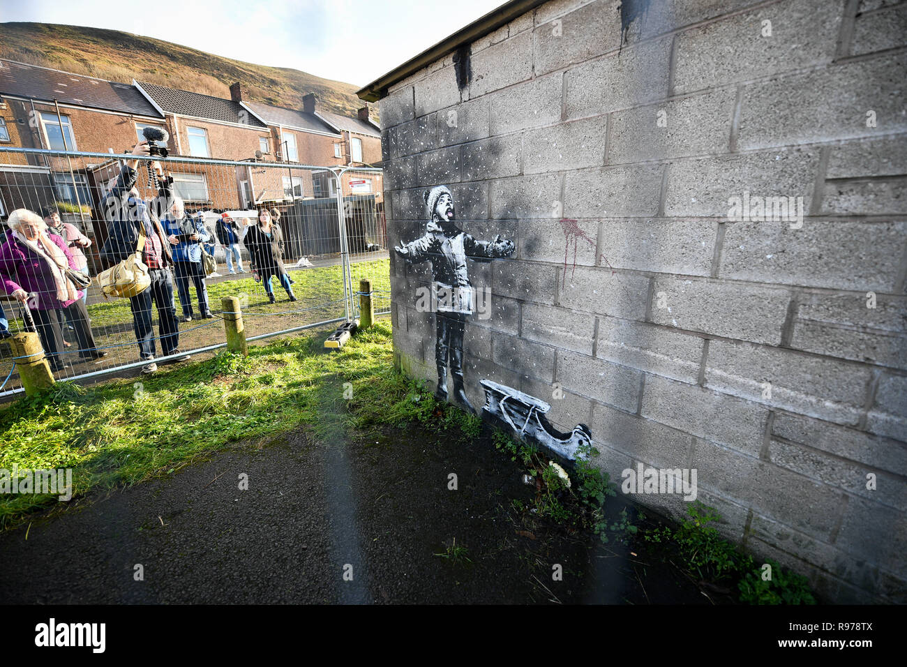 Metal fencing protects an artwork by street artist Banksy, which has appeared on a garage wall in Taibach, Port Talbot, south Wales. The painting appeared overnight and shows a child playing in the falling ash and smoke from a fire in a skip. Stock Photo