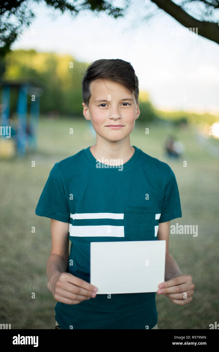 Smiling teenager with blank paper in his hand on nature in summer park. Advertising concept Stock Photo